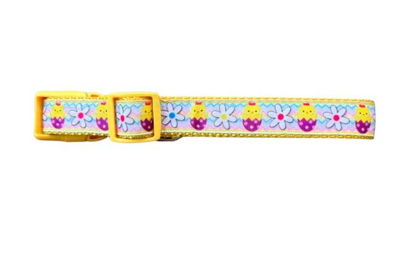 A colorful dog collar with a pattern of chicks, eggs, and daisies, predominantly yellow and purple, with a yellow plastic buckle.