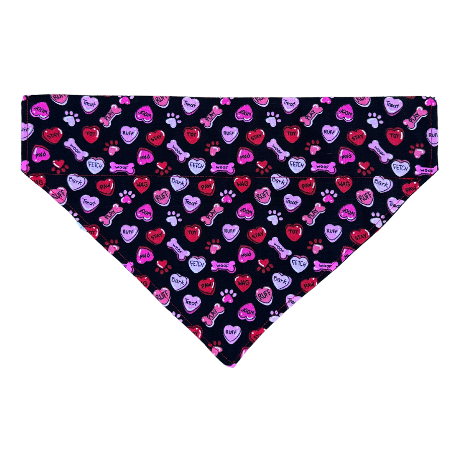 A reversible dog bandana with one side featuring black fabric with dog-themed conversation hearts.