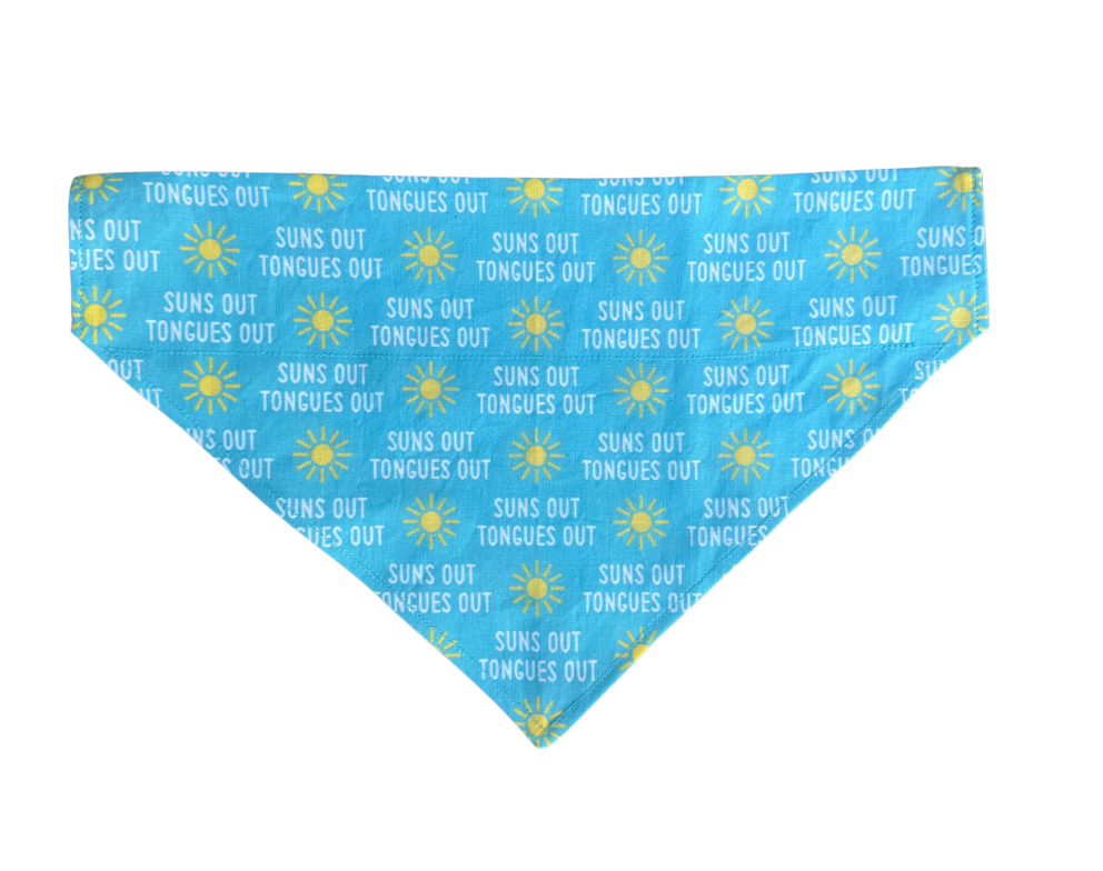 A triangular pet bandana with a light blue background, featuring a repeating pattern of yellow suns and the text 'SUNS OUT TONGUES OUT' in white, displayed on a solid white background.